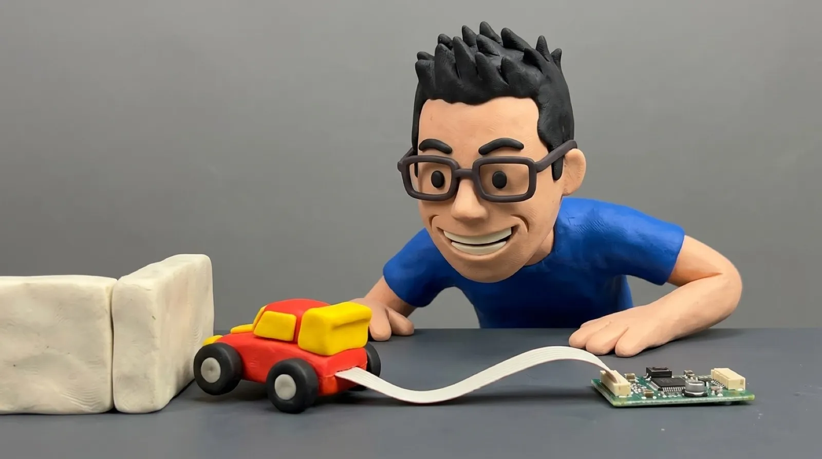 Chris crouches beside a tiny toy robot car wired to a small circuit board as it swerves